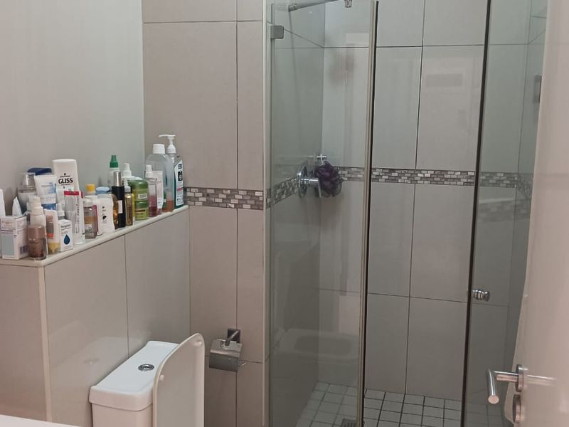 A modern bathroom featuring a glass-enclosed shower, tiled walls with decorative accents, a toilet, and a built-in vanity ledge for storage.