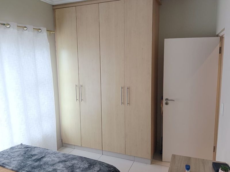 A bedroom featuring a large light wood-finish built-in wardrobe, neutral wall tones, and tiled flooring.
