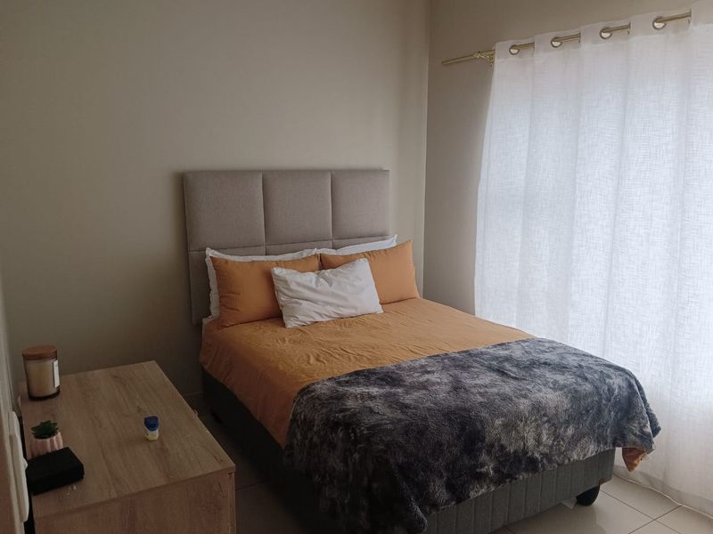 A well-maintained bedroom featuring neutral wall tones, tiled flooring, and a window dressed with a simple curtain rod.