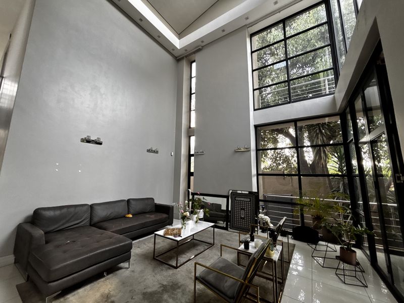 Spacious double-volume living area featuring expansive steel-framed windows that provide abundant natural light and a modern, airy atmosphere.