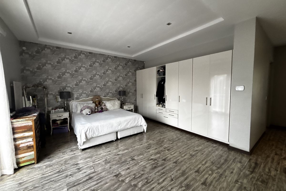 Spacious bedroom featuring modern laminate flooring, extensive built-in cupboards, recessed ceiling lighting, and a decorative feature wall.