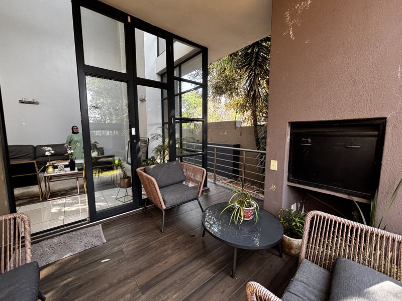 A covered patio area featuring a built-in fireplace, dark wood-look tiled flooring, and large glass doors providing seamless access to the interior living space.