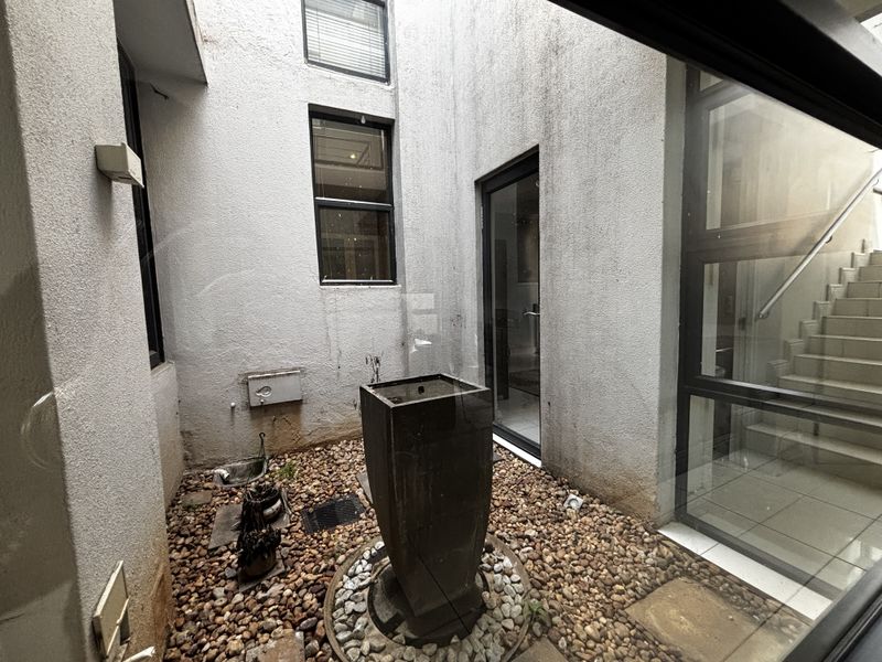 A small enclosed courtyard featuring a pebble garden, central water feature, and access to an internal staircase through glass doors.