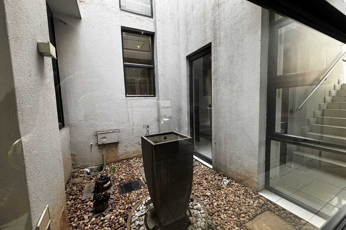 A small enclosed courtyard featuring a pebble garden, central water feature, and access to an internal staircase through glass doors.