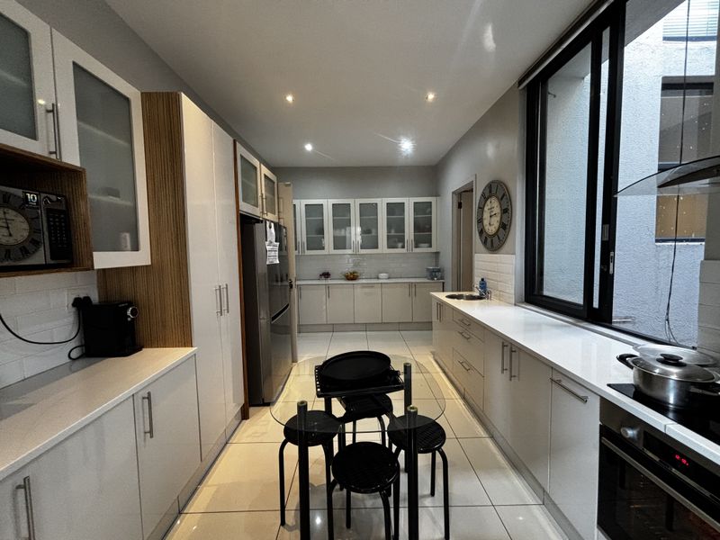 Modern galley-style kitchen featuring sleek white cabinetry, stone countertops, integrated appliances, and large windows providing natural light.