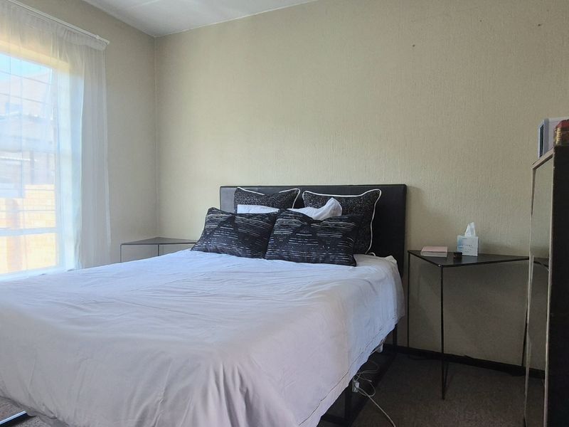 A standard bedroom featuring carpeted flooring and a window with installed curtain tracks, providing natural light to the space.