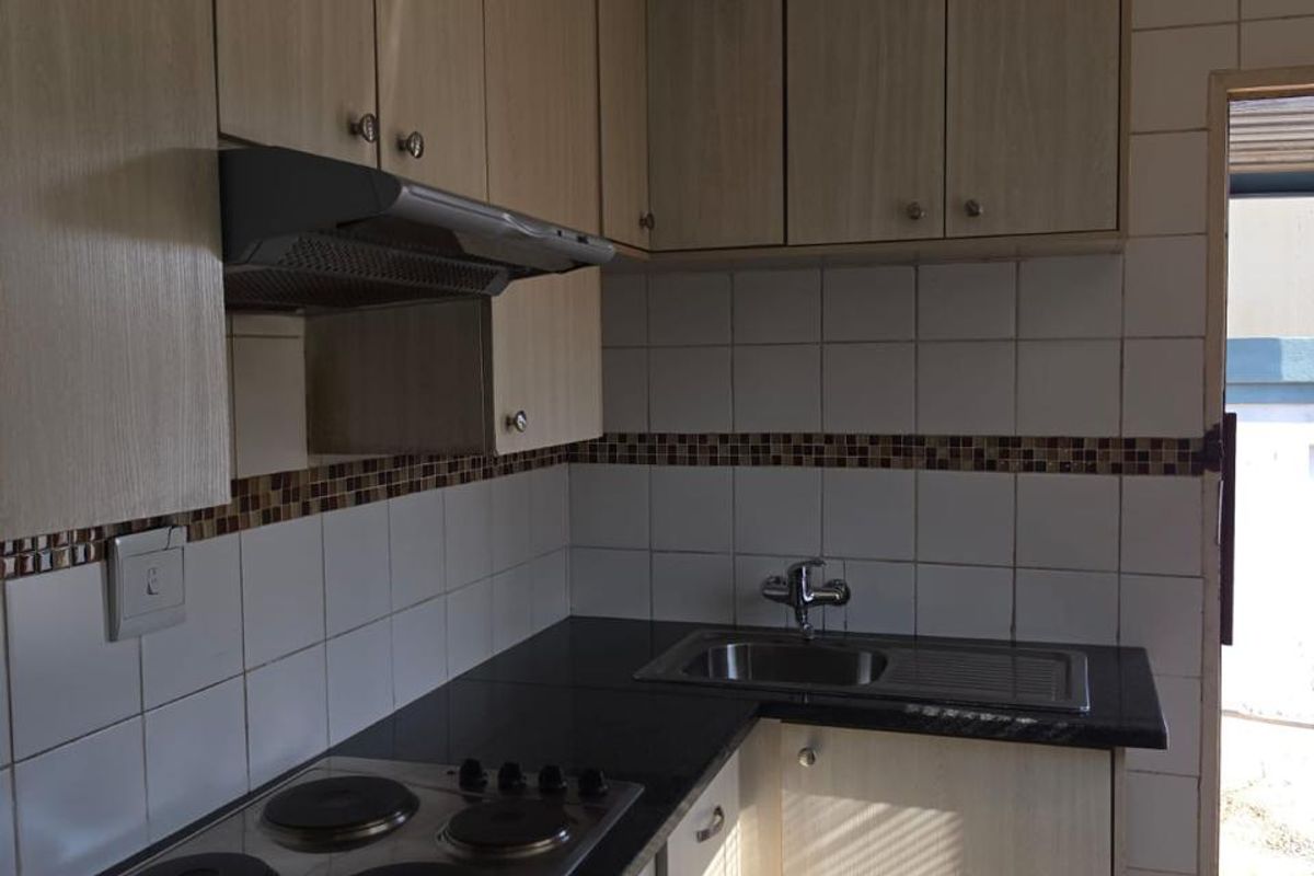 Compact kitchen featuring light wood-look cabinetry, black granite countertops, integrated electric hob, oven, and extractor fan with tiled backsplash.