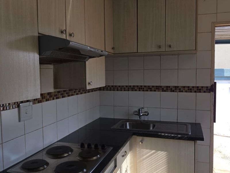 Compact kitchen featuring light wood-look cabinetry, black granite countertops, integrated electric hob, oven, and extractor fan with tiled backsplash.