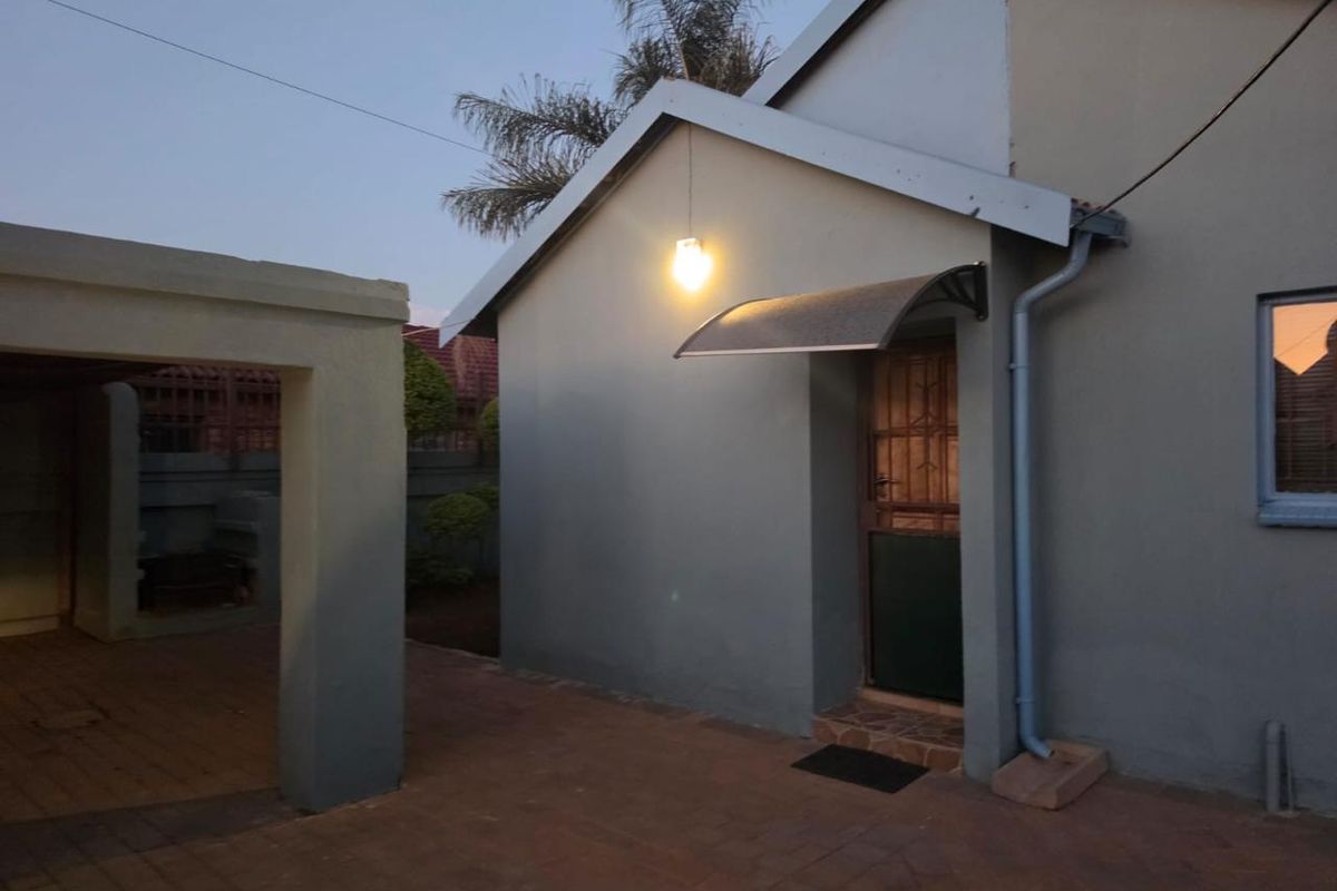 Rear exterior view showing a paved patio area, covered structure, and secure entrance door with an awning.