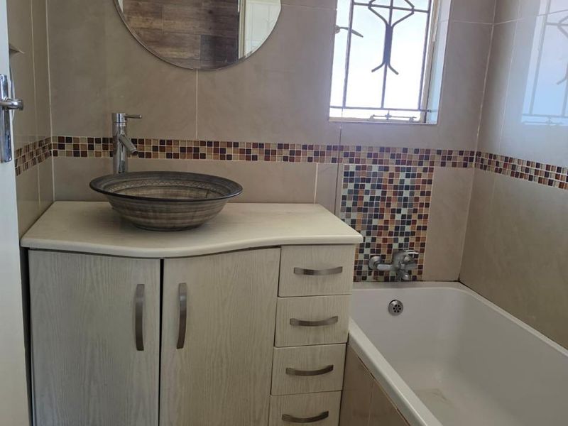 A compact bathroom featuring a vanity cabinet with a vessel sink, a bathtub, and tiled walls with decorative mosaic accents.