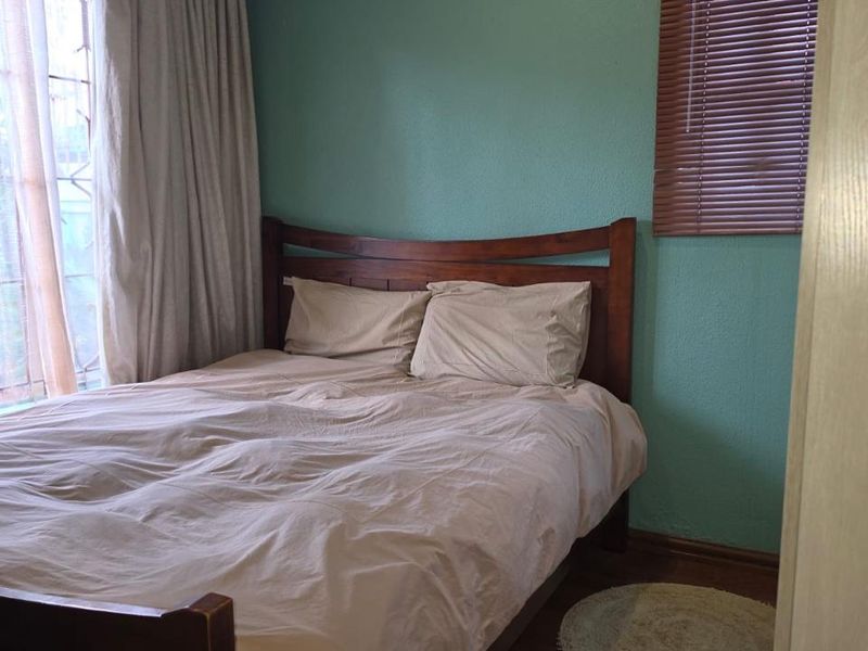 A cozy bedroom featuring laminate flooring, teal-painted walls, and window treatments including venetian blinds and curtain rails.