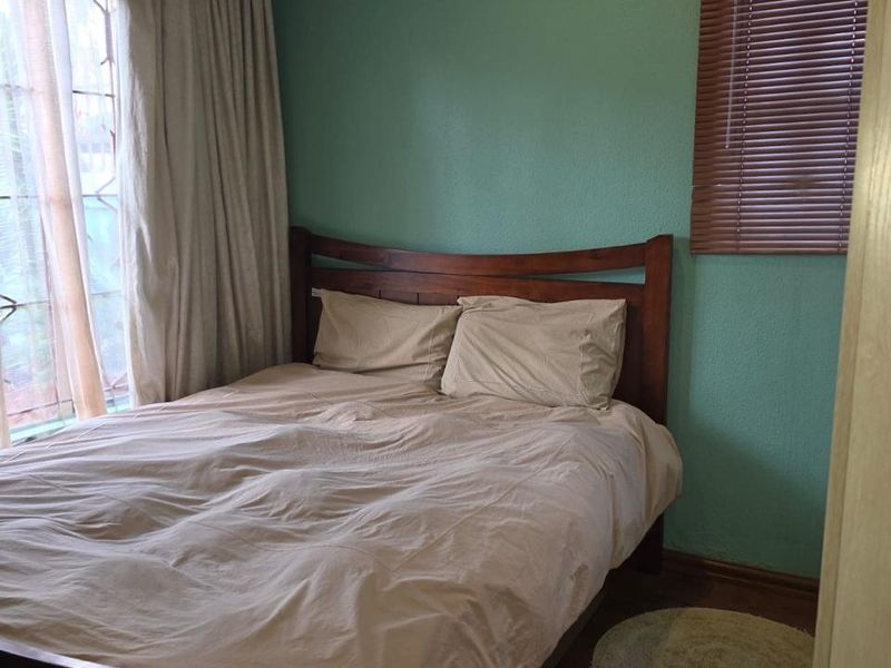 A cozy bedroom featuring laminate flooring, timber window blinds, and neutral wall tones, providing a comfortable and functional sleeping space.