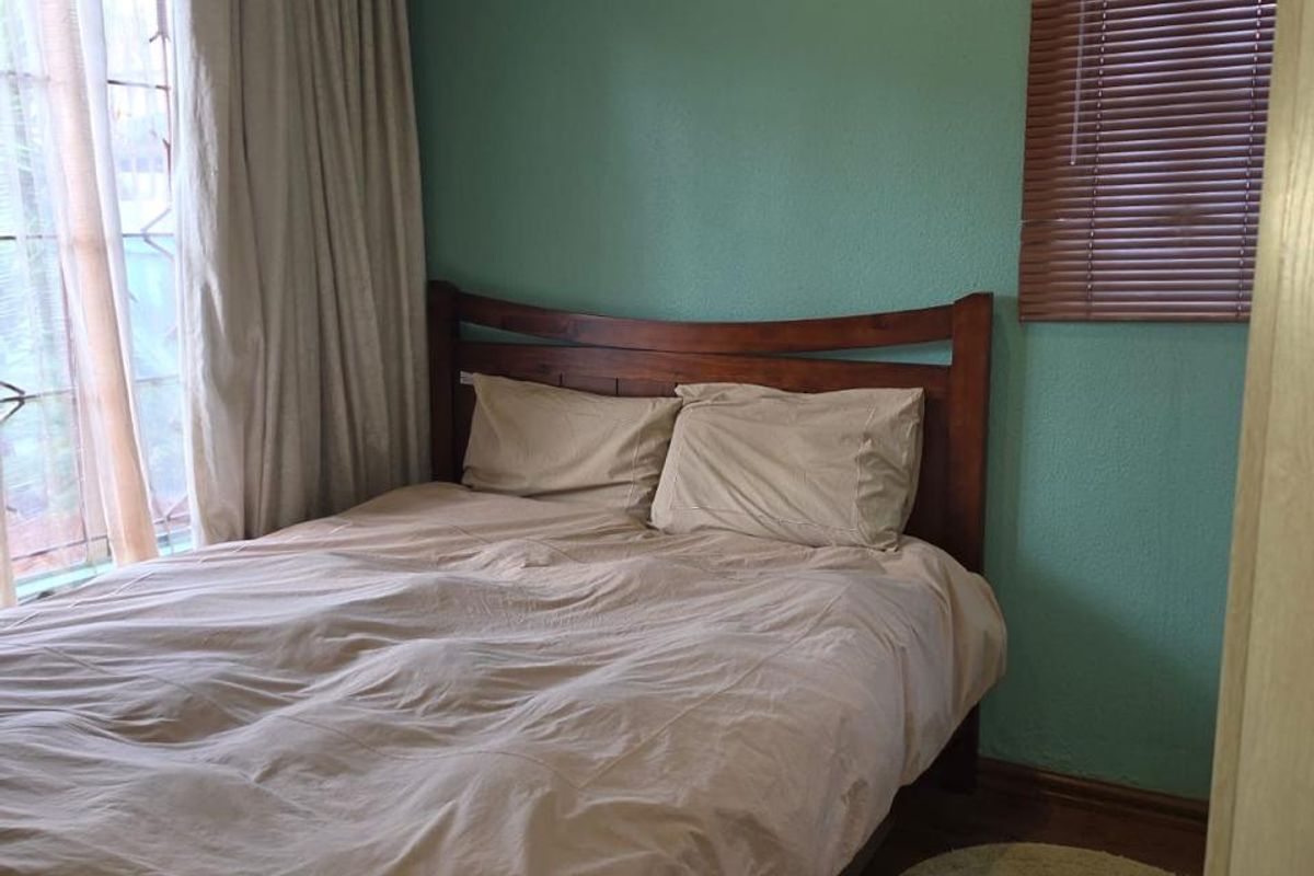 A cozy bedroom featuring laminate flooring, timber window blinds, and neutral wall tones, providing a comfortable and functional sleeping space.