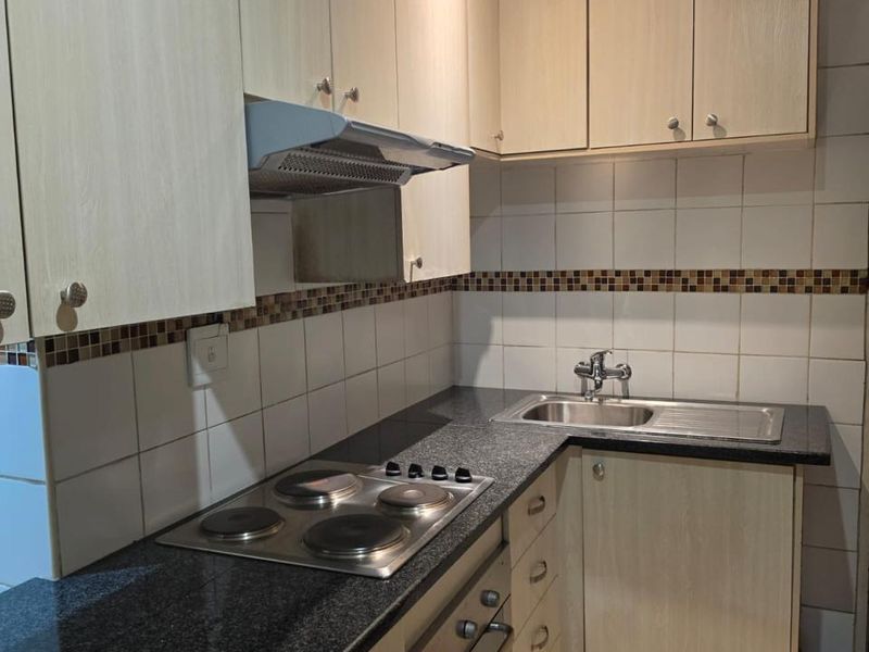 Compact kitchen featuring light wood-finish cabinetry, granite countertops, a built-in oven, electric hob, and a tiled backsplash.
