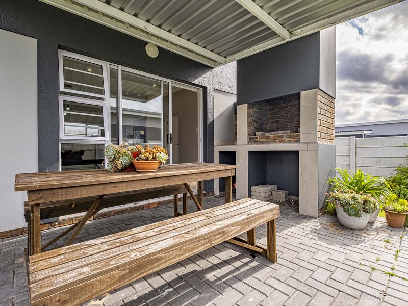 Covered outdoor patio featuring a built-in brick braai, paved flooring, and direct access to the interior through sliding glass doors.