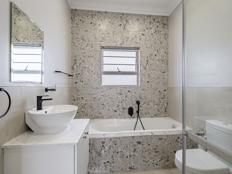 Modern bathroom featuring terrazzo wall tiling, a built-in bathtub, a vanity with a countertop basin, and contemporary black fixtures.