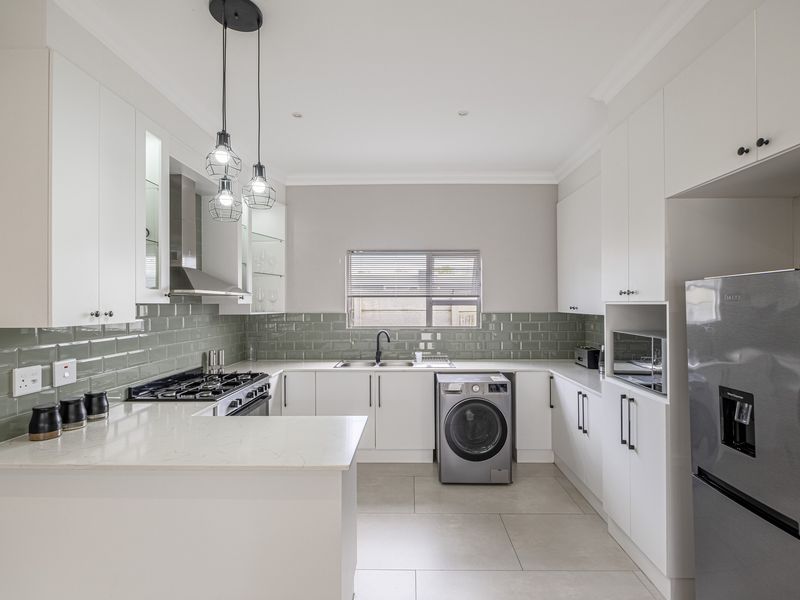 Modern kitchen featuring white cabinetry, quartz countertops, subway tile backsplash, gas hob, extractor fan, and integrated laundry plumbing.