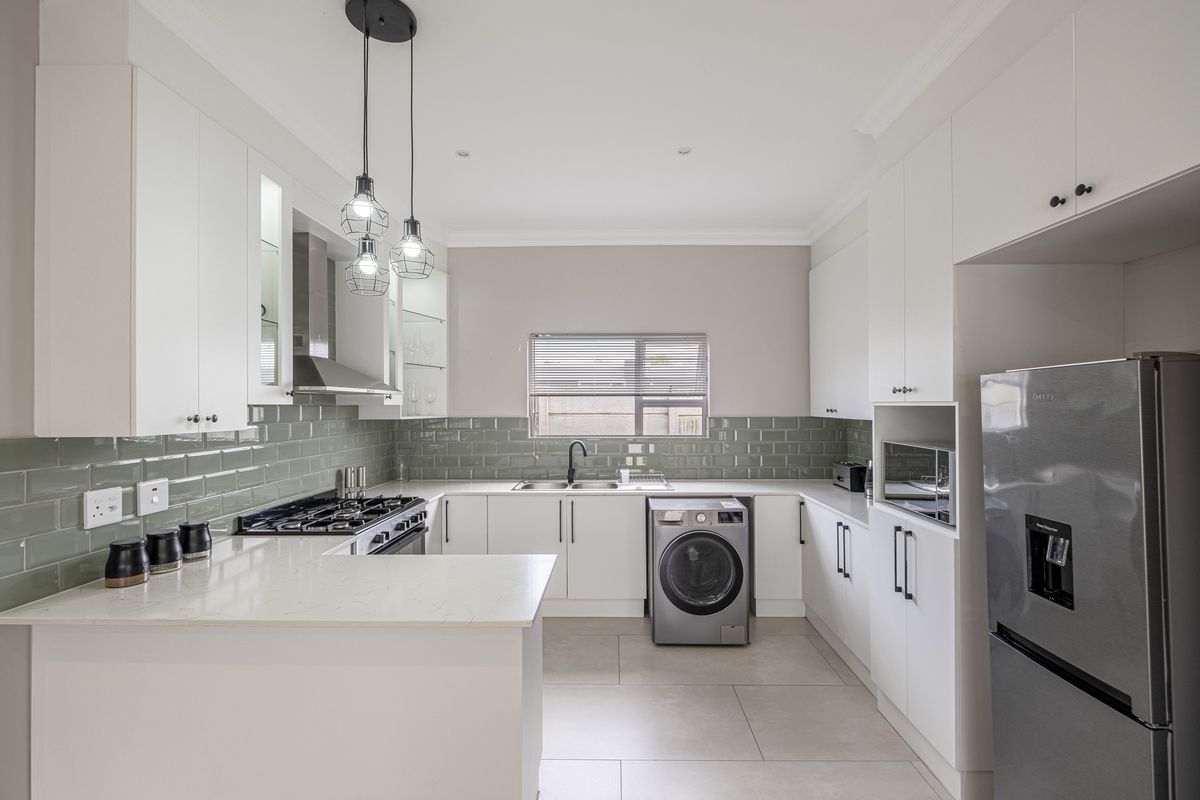 Modern kitchen featuring white cabinetry, quartz countertops, subway tile backsplash, gas hob, extractor fan, and integrated laundry plumbing.