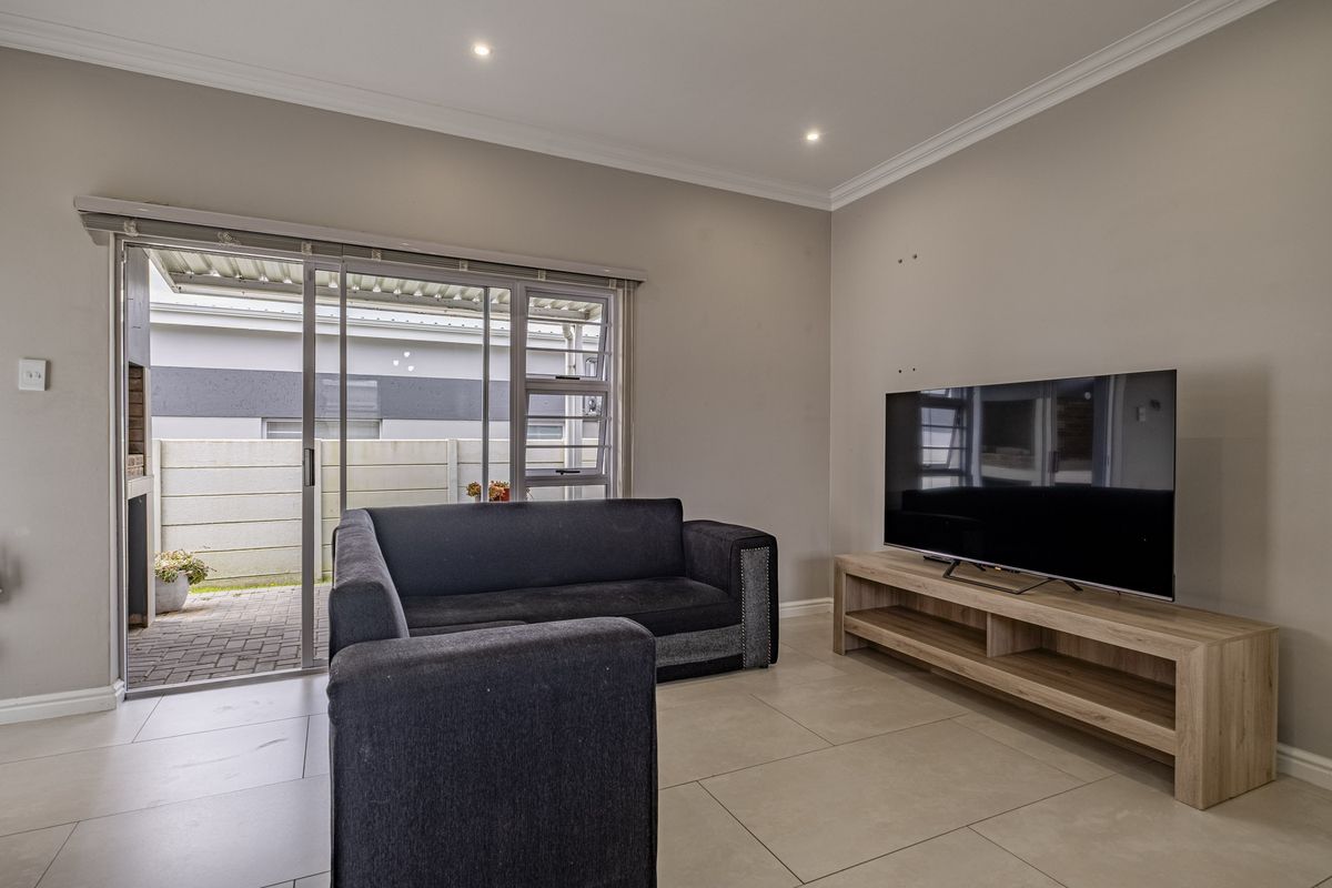 A well-maintained living room featuring tiled flooring, recessed downlights, and a sliding glass door providing access to the outdoor patio area.