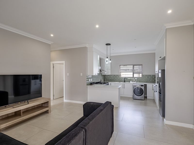 Modern open-plan living area featuring a well-appointed kitchen with stone countertops, subway tile backsplash, and integrated gas hob, flowing into a spacious lounge.