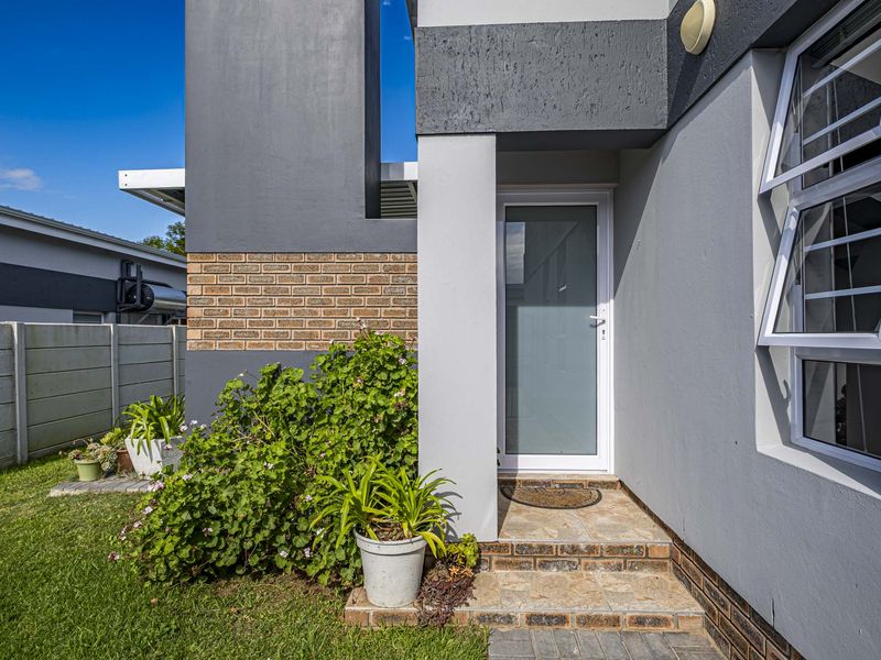 Modern townhouse entrance featuring a frosted glass door, brick accent detailing, and a tiled step leading to a well-maintained garden area.
