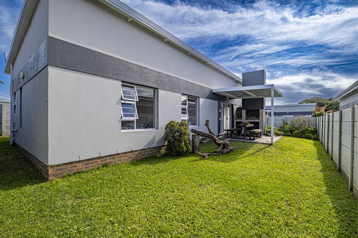 Rear view of the townhouse featuring a well-maintained lawn, a covered patio area with a built-in braai, and secure boundary walling.