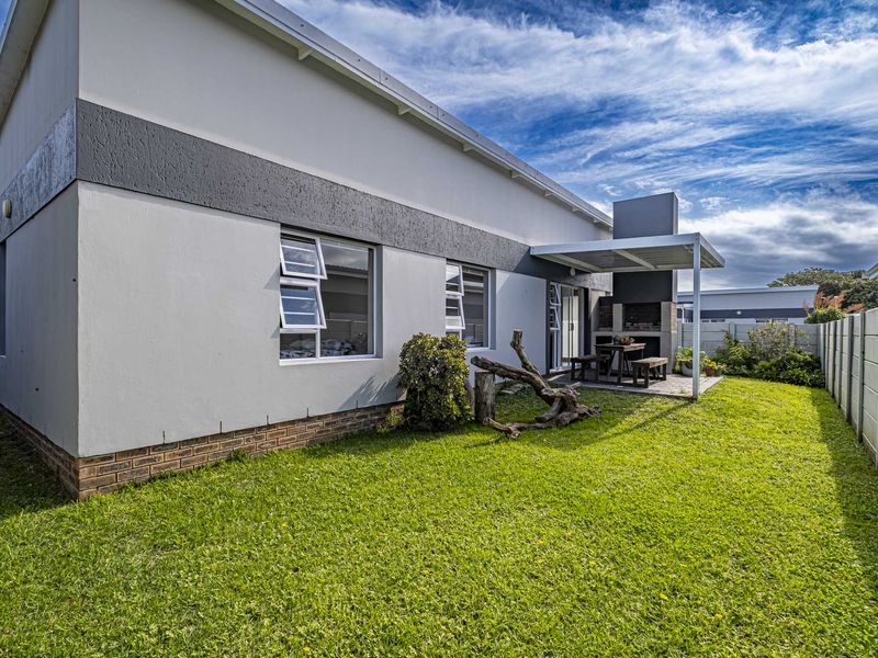 Rear view of the townhouse featuring a well-maintained lawn, a covered patio area with a built-in braai, and secure boundary walling.