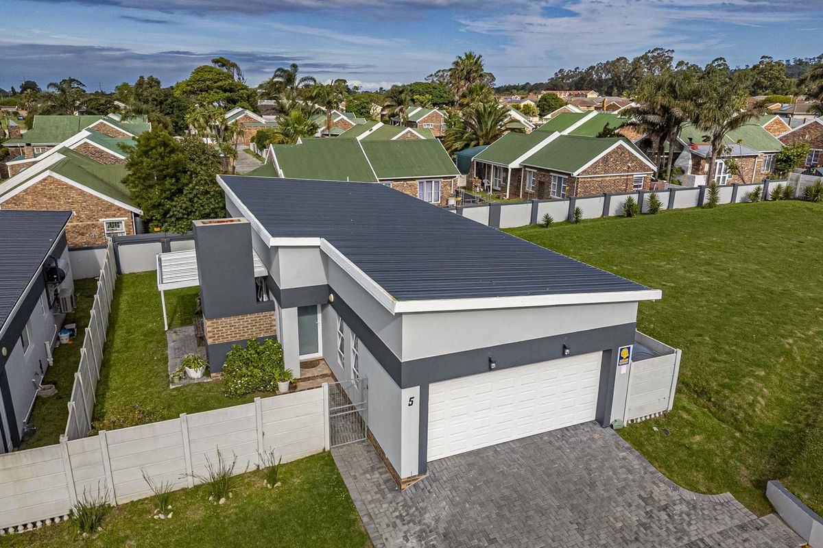 Aerial view of a modern townhouse featuring a metal roof, double garage, paved driveway, and private garden area within a secure residential complex.