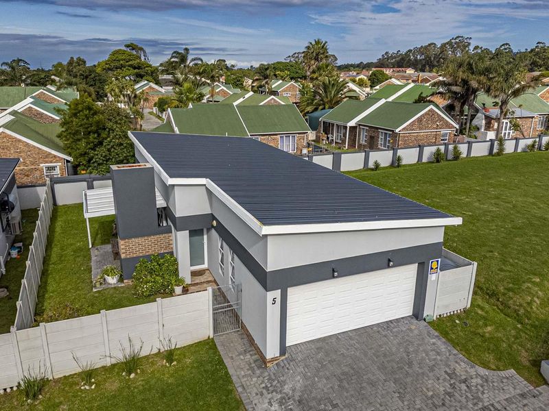 Aerial view of a modern townhouse featuring a metal roof, double garage, paved driveway, and private garden area within a secure residential complex.