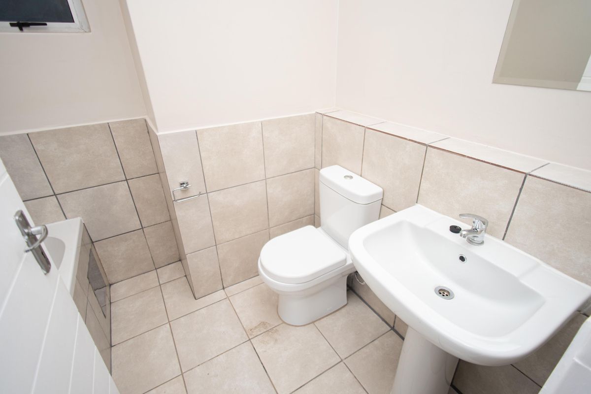 A functional bathroom featuring a pedestal washbasin, toilet, and bathtub with neutral wall and floor tiling.