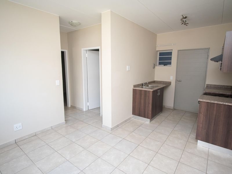 An open-plan living and kitchen area featuring neutral tiled flooring, modern wood-finish cabinetry, and a functional layout with direct access to adjacent rooms.
