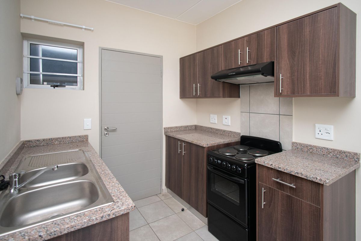 A functional kitchen featuring dark wood-look cabinetry, granite countertops, a double stainless steel sink, and a built-in electric stove with an extractor fan.