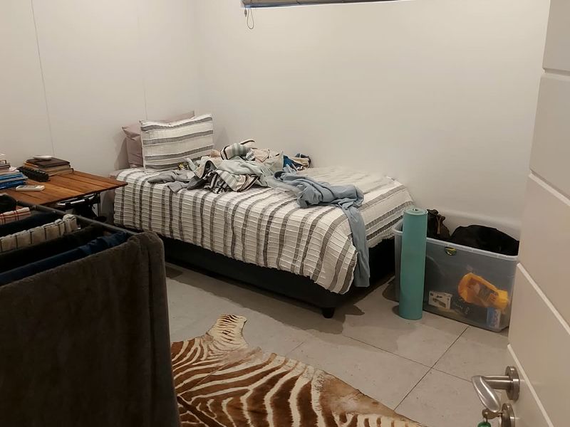 A functional bedroom featuring neutral tiled flooring, recessed lighting, and a horizontal window with fitted venetian blinds.
