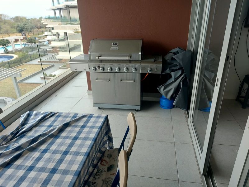 A spacious balcony featuring tiled flooring, a glass balustrade, and sliding door access, offering a functional outdoor area for relaxation and dining.