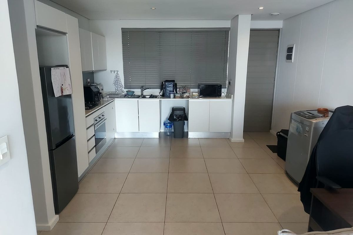 Modern kitchen featuring white cabinetry, integrated oven, tiled flooring, and large window with venetian blinds, offering a clean and functional workspace.