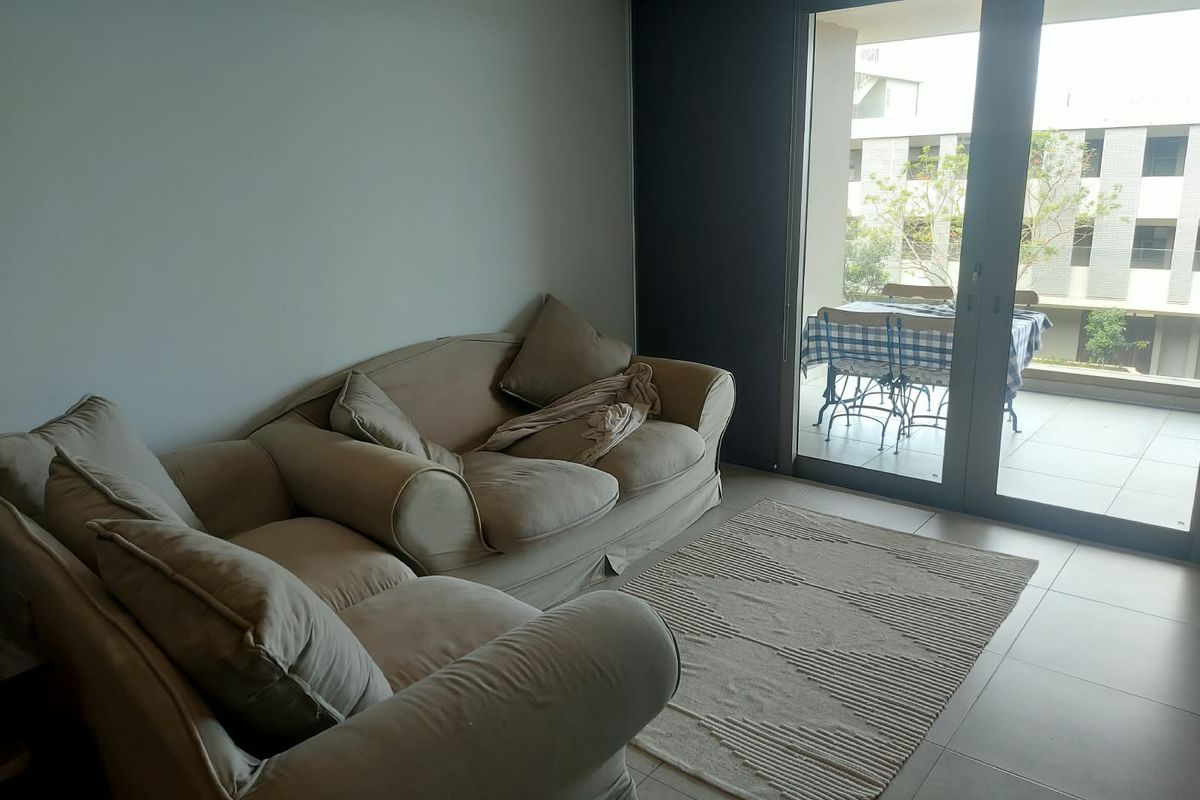 A bright living room featuring large sliding glass doors that open onto a private balcony, with neutral tiled flooring throughout.