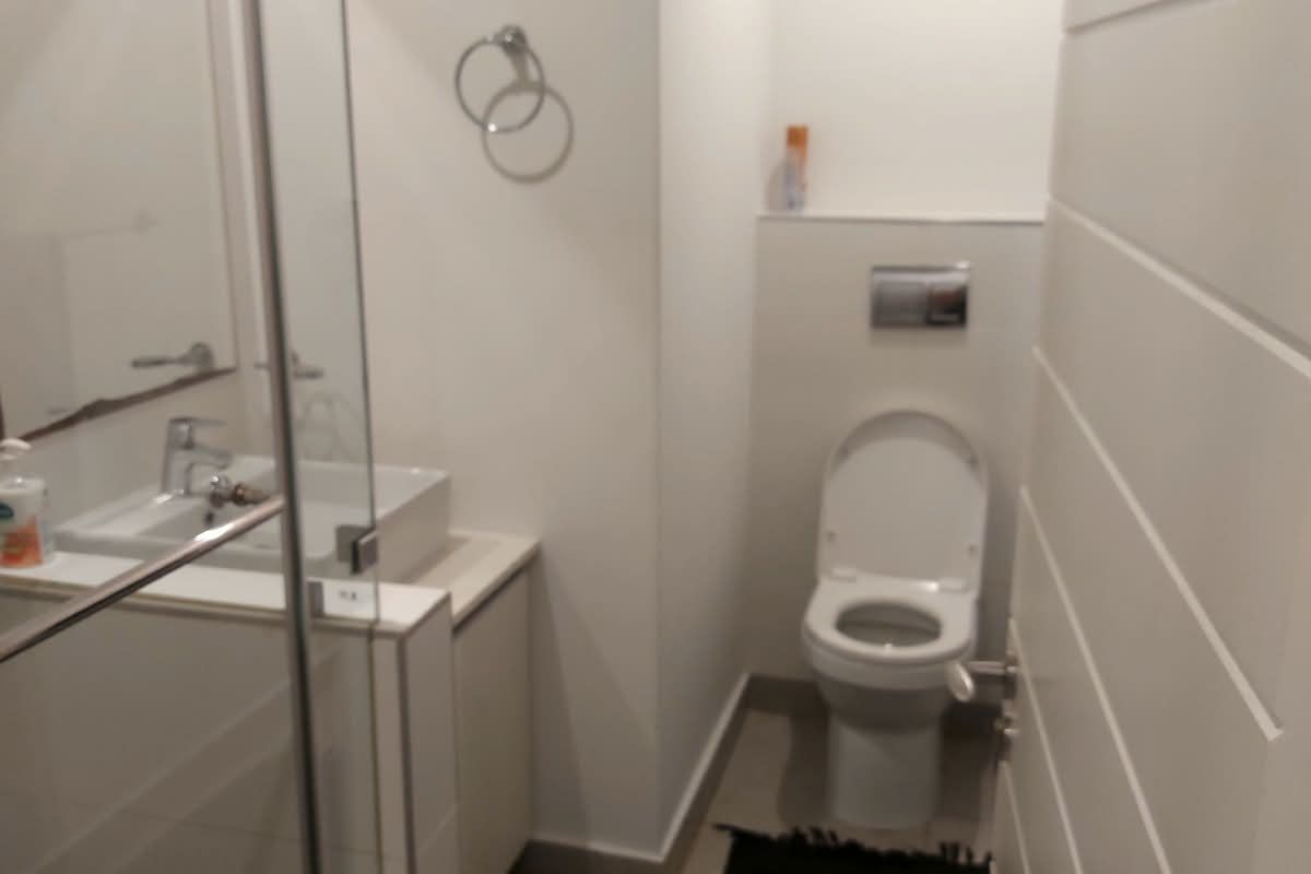 A modern, clean bathroom featuring a wall-mounted toilet, a glass-enclosed shower, and a sleek vanity basin with chrome fixtures.