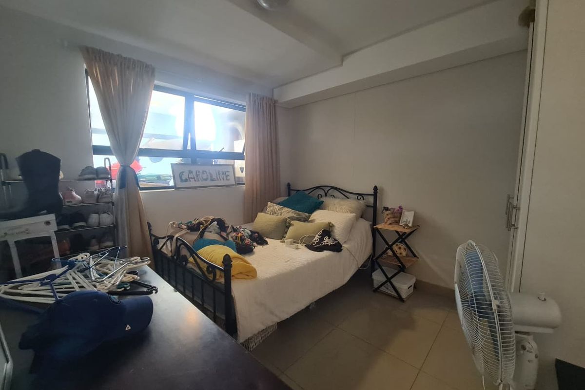 A functional bedroom featuring tiled flooring, a built-in wardrobe, and an aluminium-framed window providing natural light.