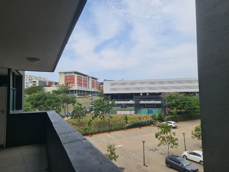 A view from a private balcony overlooking the surrounding neighborhood, parking area, and nearby commercial buildings.