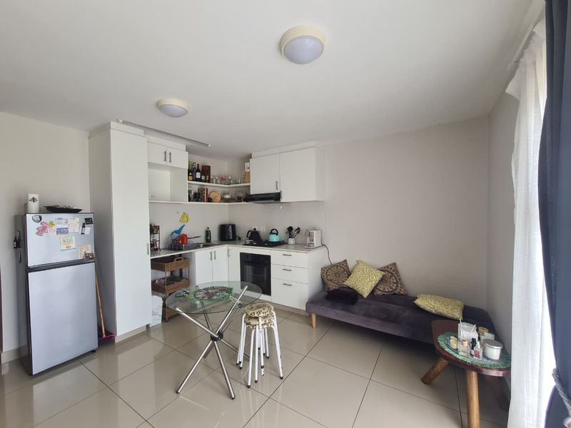 Compact open-plan living area featuring a functional kitchen with white cabinetry, built-in oven, hob, and tiled flooring throughout.