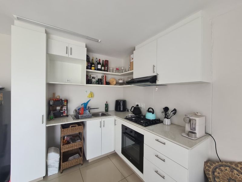A compact, modern kitchen featuring white cabinetry, stone countertops, a gas hob, built-in oven, and an extractor fan, finished with neutral floor tiles.