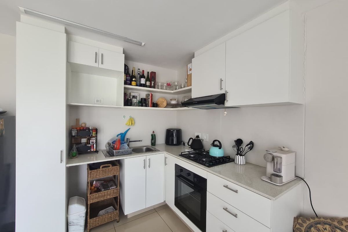A compact, modern kitchen featuring white cabinetry, stone countertops, a gas hob, built-in oven, and an extractor fan, finished with neutral floor tiles.