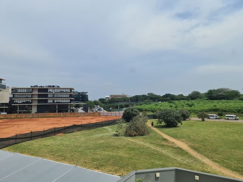 An elevated view overlooking a green field, adjacent construction site, and surrounding neighborhood infrastructure.