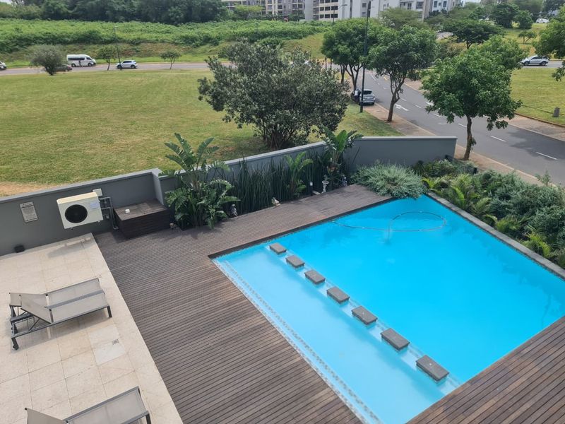 An elevated view of a private swimming pool area featuring timber decking, stone paving, and integrated stepping stones within the pool.