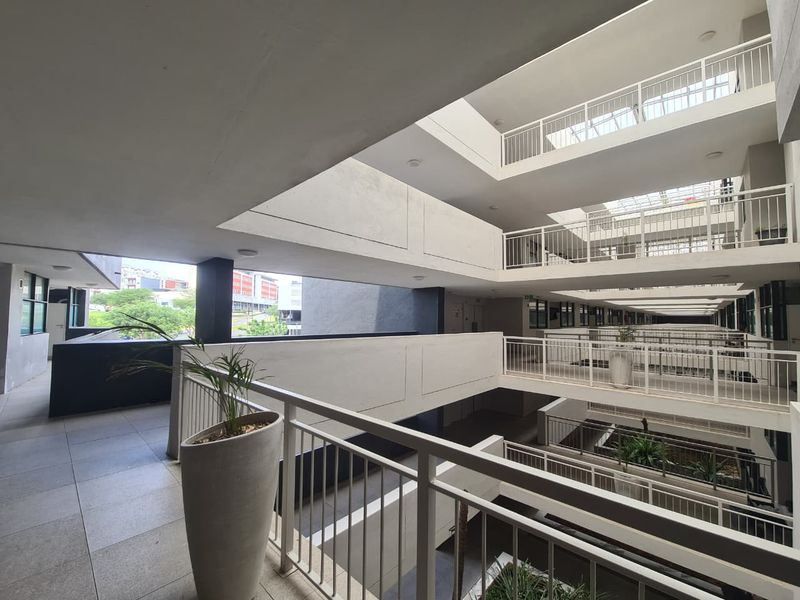 A modern, multi-level apartment complex hallway featuring open-air atrium design, tiled walkways, and secure metal balustrades.