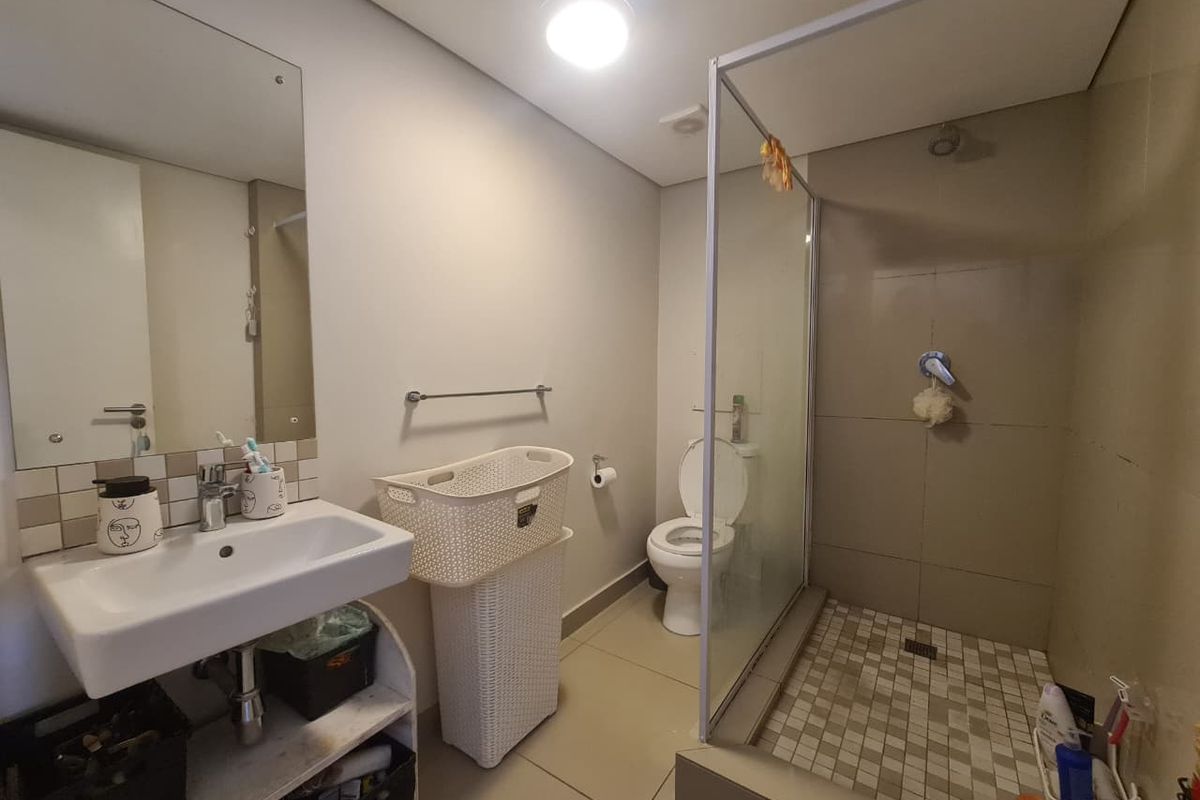 A functional bathroom featuring a wall-mounted basin, a glass-enclosed shower with tiled flooring, and a standard toilet, finished with neutral wall tiles.