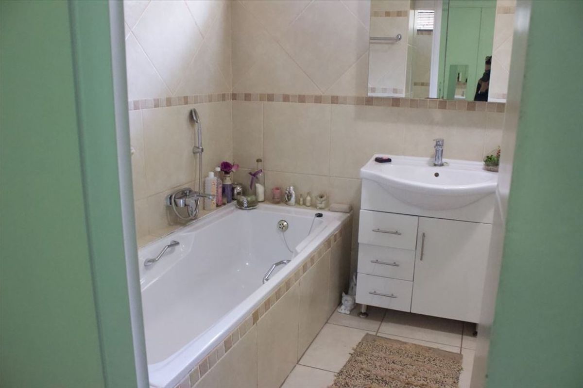 A functional bathroom featuring a built-in bathtub with shower mixer, a vanity cabinet with basin, and neutral wall tiling.