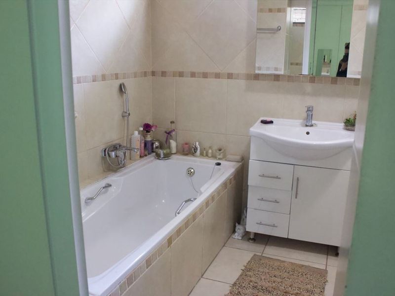 A functional bathroom featuring a built-in bathtub with shower mixer, a vanity cabinet with basin, and neutral wall tiling.