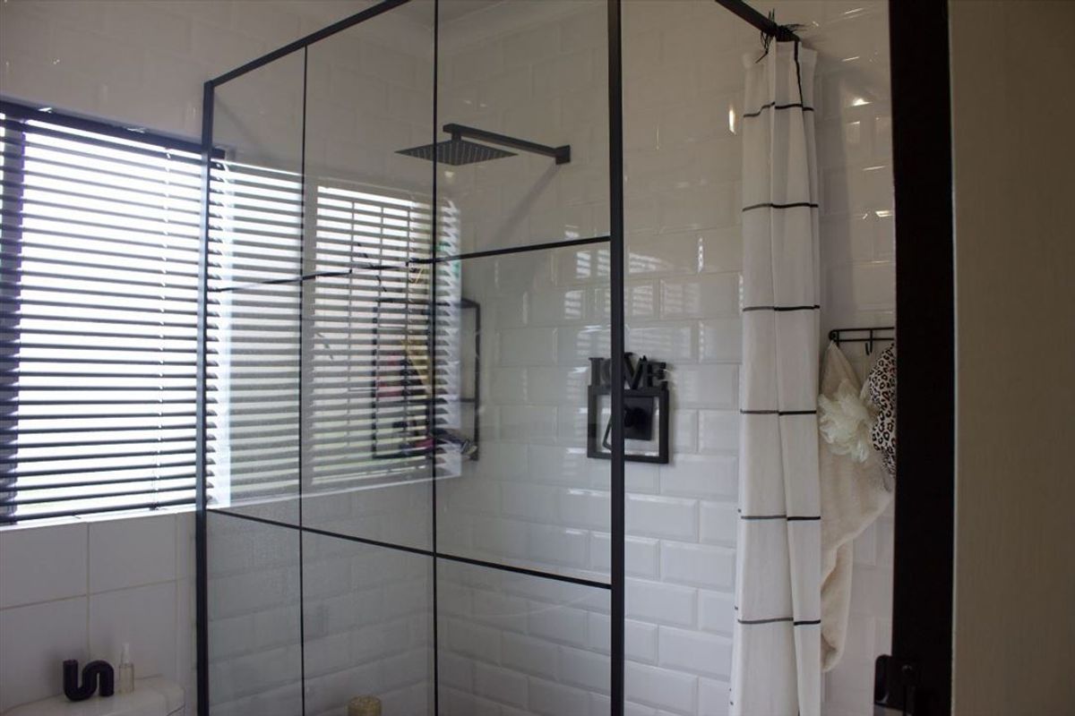 Modern bathroom featuring a walk-in shower with a black-framed glass screen, subway tile wall finishes, and a contemporary rain shower head.