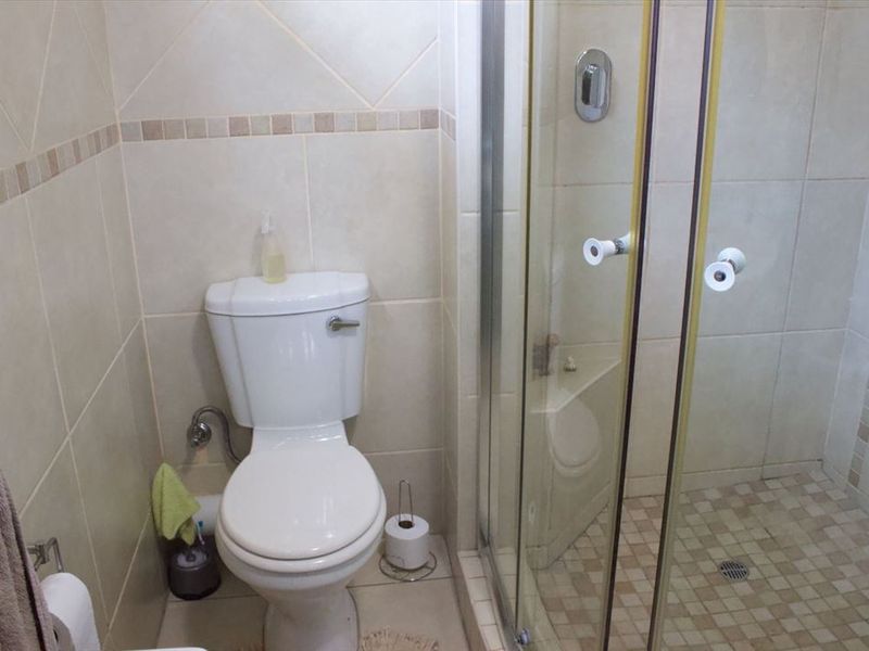 A compact bathroom featuring a standard toilet and a glass-enclosed shower with neutral wall and floor tiling.